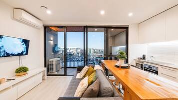 A modern living space with a sofa, a wooden dining table, a TV, and a kitchen area.