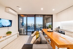 A modern living space with a sofa, a wooden dining table, a TV, and a kitchen area.