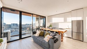 En moderne lejlighed med balkon, en grå sofa, et træspisebord og et køkkenområde.