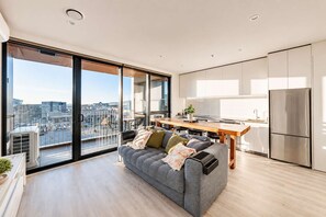 Un apartamento moderno con balcón, un sofá gris, una mesa de comedor de madera y una zona de cocina.