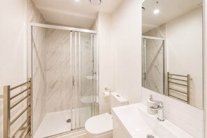 Een moderne badkamer met een douchecabine van glas, een wit toilet en een wastafel met spiegel.