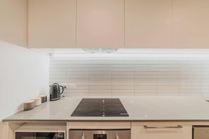 Een moderne keuken met een wit aanrecht, een zwart inductiefornuis en een roestvrijstalen oven.