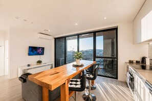 A modern kitchen with a wooden island, black chairs, a potted plant, and a large window with a city view.