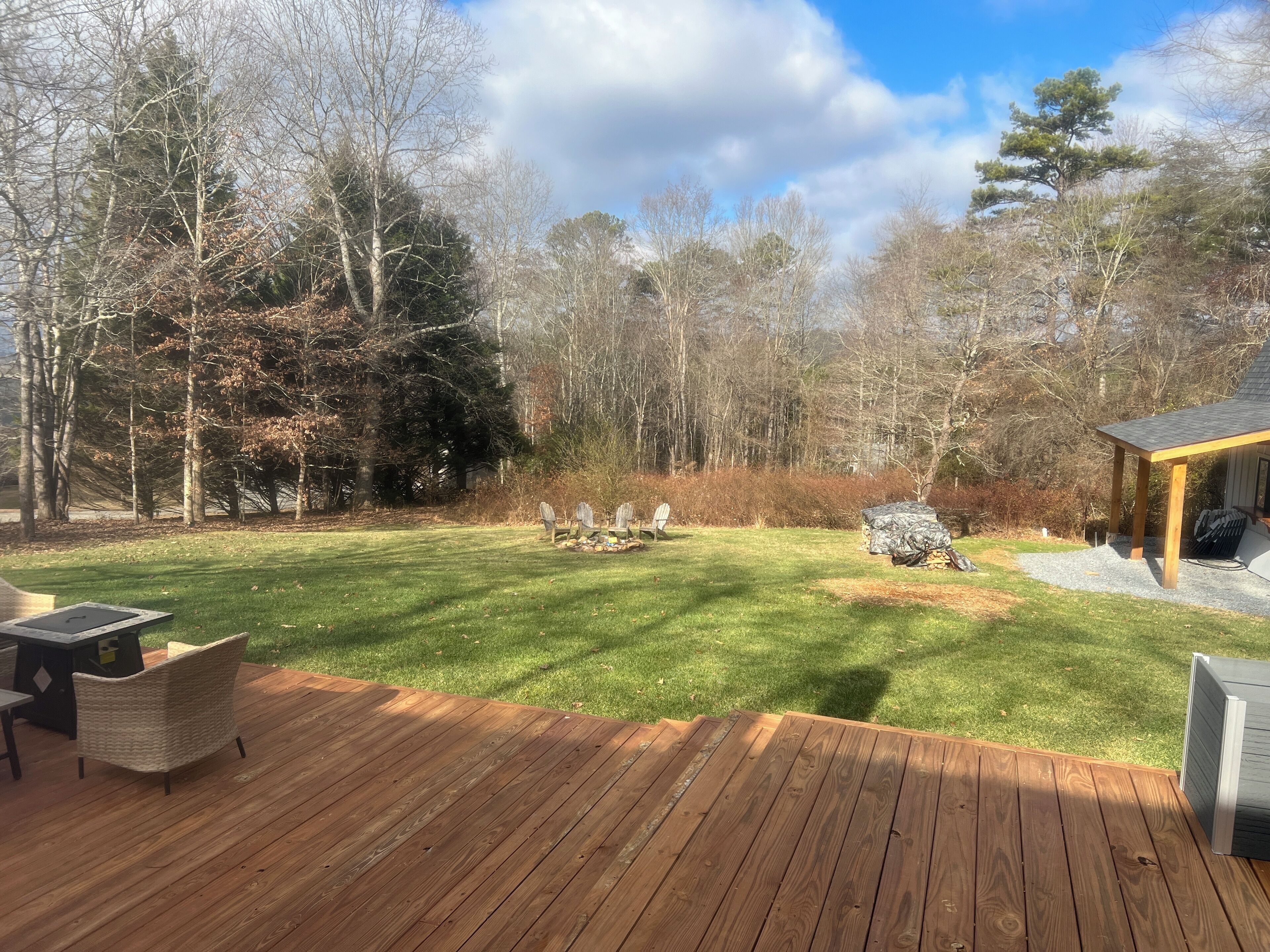 A wooden deck with outdoor furniture, a grassy yard, and a wooded area in the background.