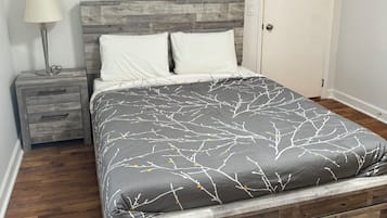 A bed with a gray and white patterned bedspread, a wooden headboard, and a framed artwork of a bull's head above it.