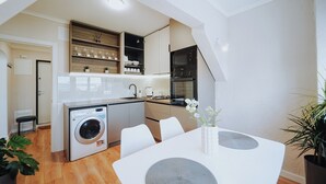 Une cuisine compacte équipée d’un lave-linge, d’un coin repas avec une table et des chaises, et d’un petit banc.