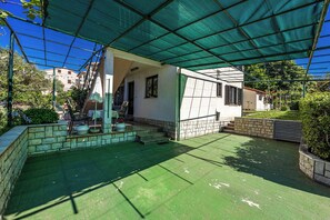 Un espacio al aire libre cubierto con techo verde, escalones de piedra y un pequeño edificio con ventanas.