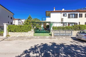 Una calle residencial con un edificio blanco, un acceso verde y un autom óvil estacionado.