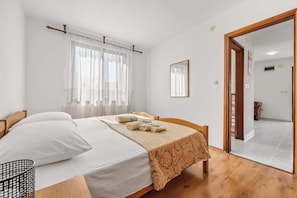 A bedroom with a bed, a bedside table, a window with curtains, a mirror on the wall, and a wooden floor. - Koreni A2 one bedroom apartment in Rovinj (Rovinj)