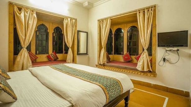 A hotel room with two beds, each with a canopy, a television, and a large mirror.