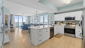 A spacious kitchen with white cabinets, a stainless steel refrigerator, and a built-in oven. - Sandy shores await! Book this 3/3 Sleeping 7 NOW! (Navarre)