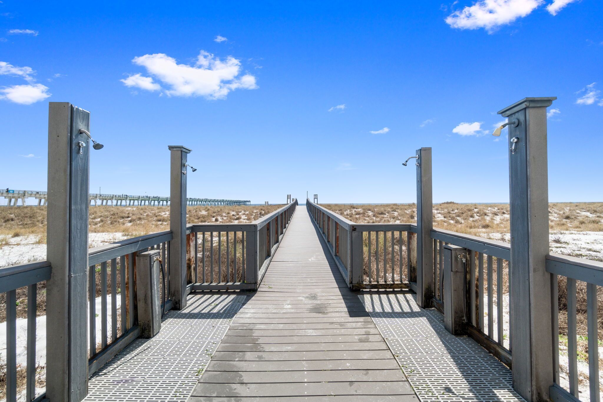 A wooden boardwalk leading to a beach with a pier in the background.