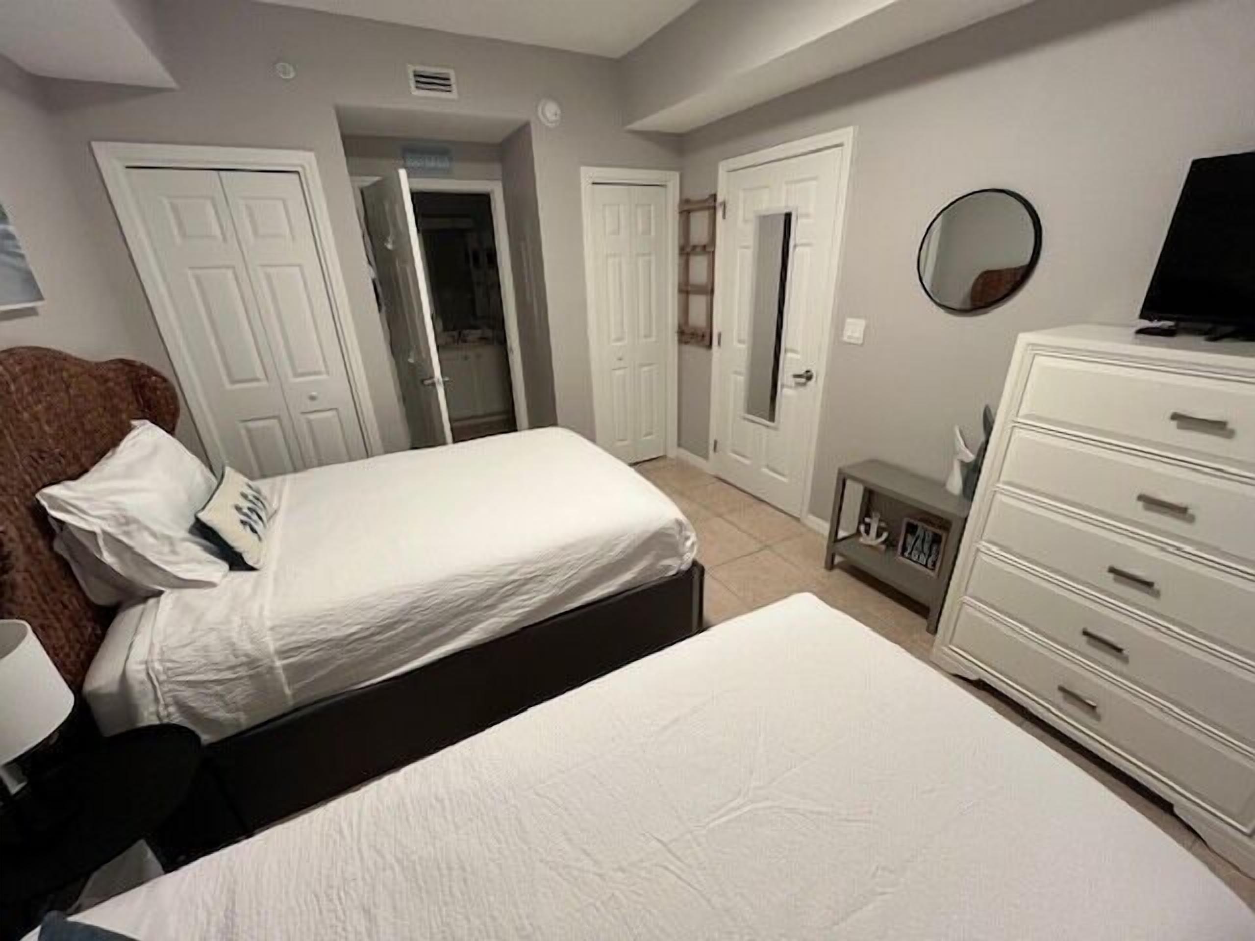 A bedroom with two beds, a dresser, a mirror, and a door leading to another room.