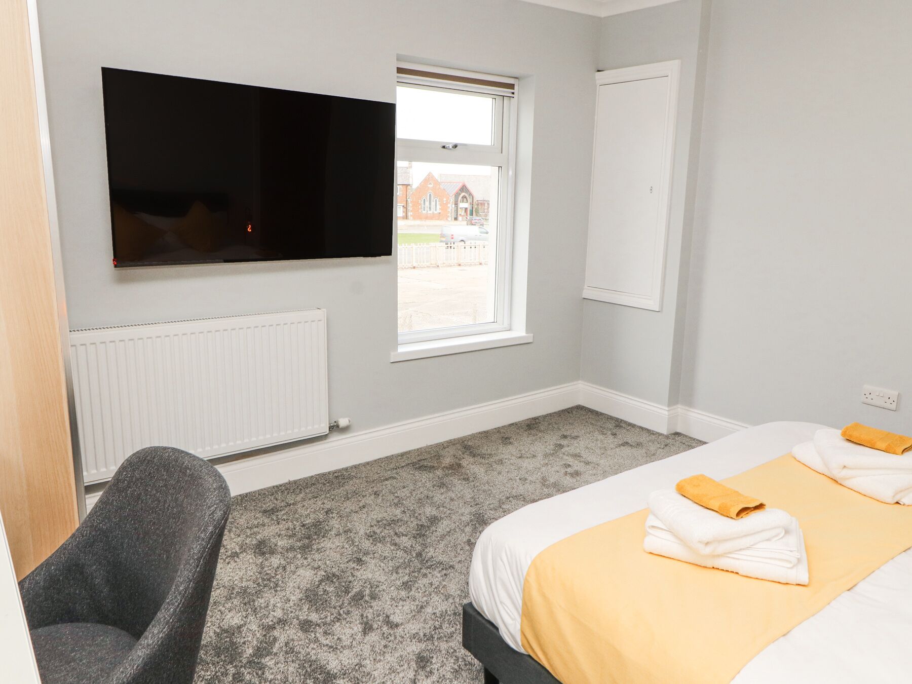 Ein Hotelzimmer mit Bett, Sessel, Fernseher, Fenster und Heizkörper.