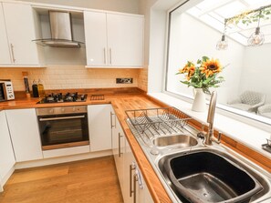 A modern kitchen with white cabinets, a stainless steel sink, and a window with a view of the outdoors. - Grace House (Wigton)