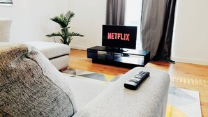 A living room with a grey sofa, a black TV stand, and a remote control on the sofa.