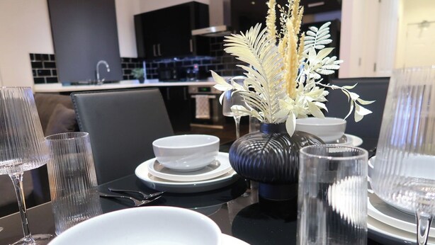 Una mesa de comedor dispuesta con cuencos blancos, vasos transparentes y un jarrón decorativo.