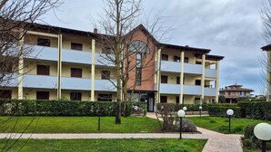 En flerlags boligbygning med altaner, en central indgang og en velholdt have med sti.
