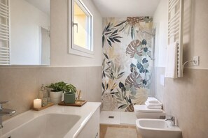 Ein modernes Badezimmer mit Badewanne, Dusche, Waschbecken und Toilette. Über der Dusche befindet sich ein Fenster, und die Wände sind mit einem Blattmuster dekoriert.