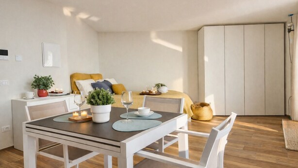 A modern, well-lit room with a dining table set for two, a bed with yellow bedding, a small potted plant, and a wardrobe. - La Gialla (Attico d'Amore) By Case al Lago (Padenghe sul Garda)