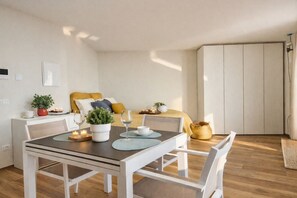 A modern, well-lit room with a dining table set for two, a bed with yellow bedding, a small potted plant, and a wardrobe. - La Gialla (Attico d'Amore) By Case al Lago (Padenghe sul Garda)