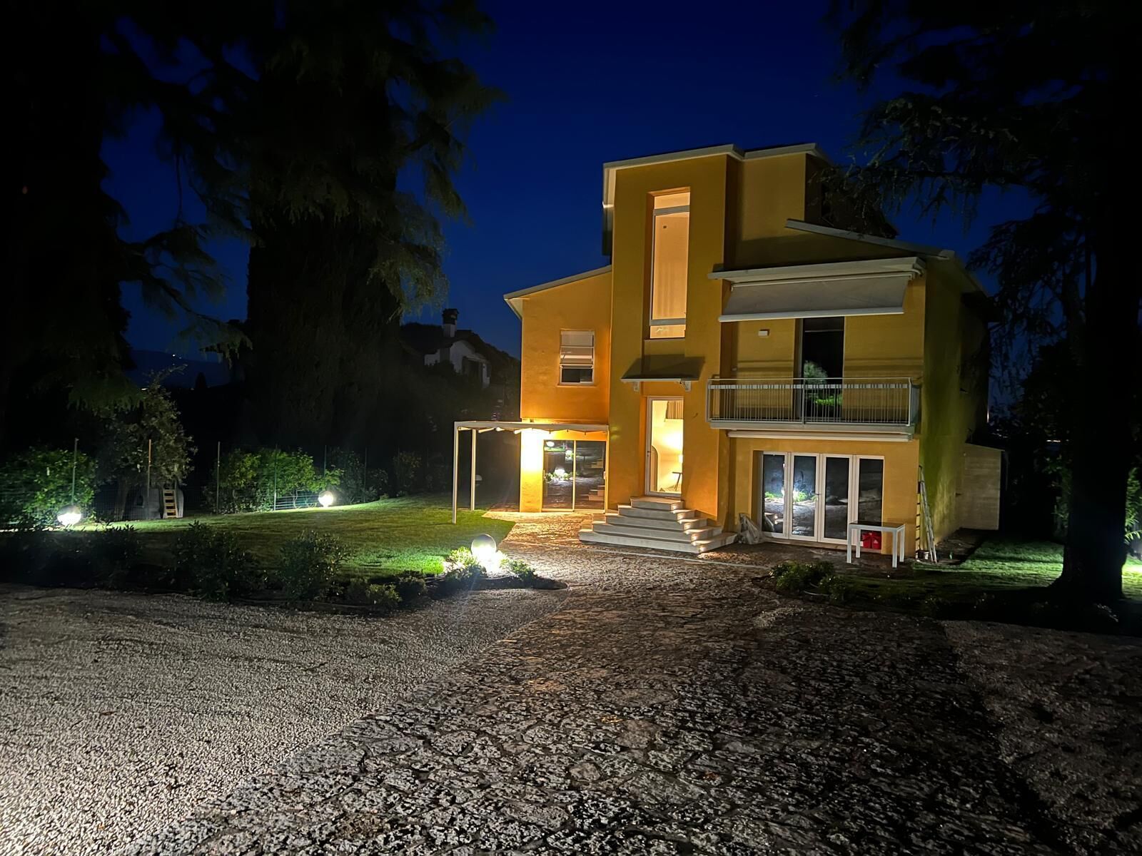 A modern two-story house with a well-lit entrance and a gravel driveway.