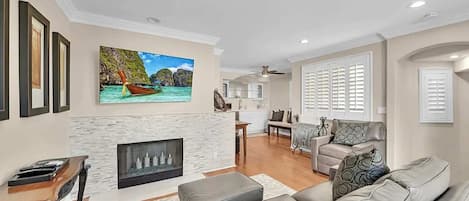 A living room with a fireplace, a sofa, and a dining area in the background.