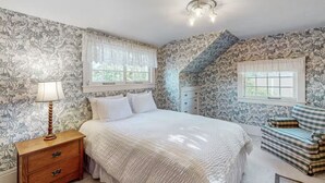 A bedroom with a bed, a dresser, a lamp, and two windows.