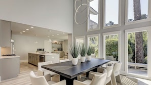 A modern kitchen with white cabinets, a central island, and a dining area with a dark table and white chairs. - Sunset Rentals | Red Oak 40 (Hilton Head Island)
