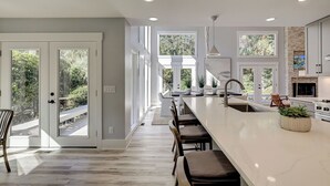 A modern kitchen with a large island, bar stools, and a view of the outdoors. - Sunset Rentals | Red Oak 40 (Hilton Head Island)