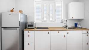 Een keuken met witte kastjes, een roestvrijstalen koelkast, een broodrooster en een raam met jaloezieën.