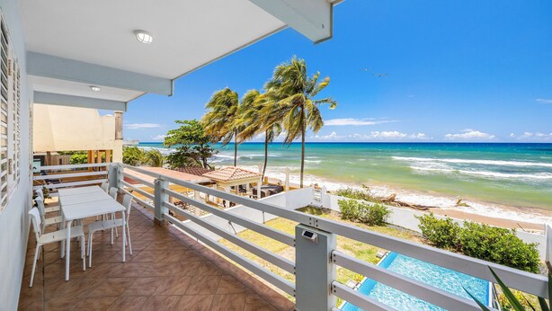Een balkon met uitzicht op het strand, een zwembad en een eethoek met stoelen en tafels.