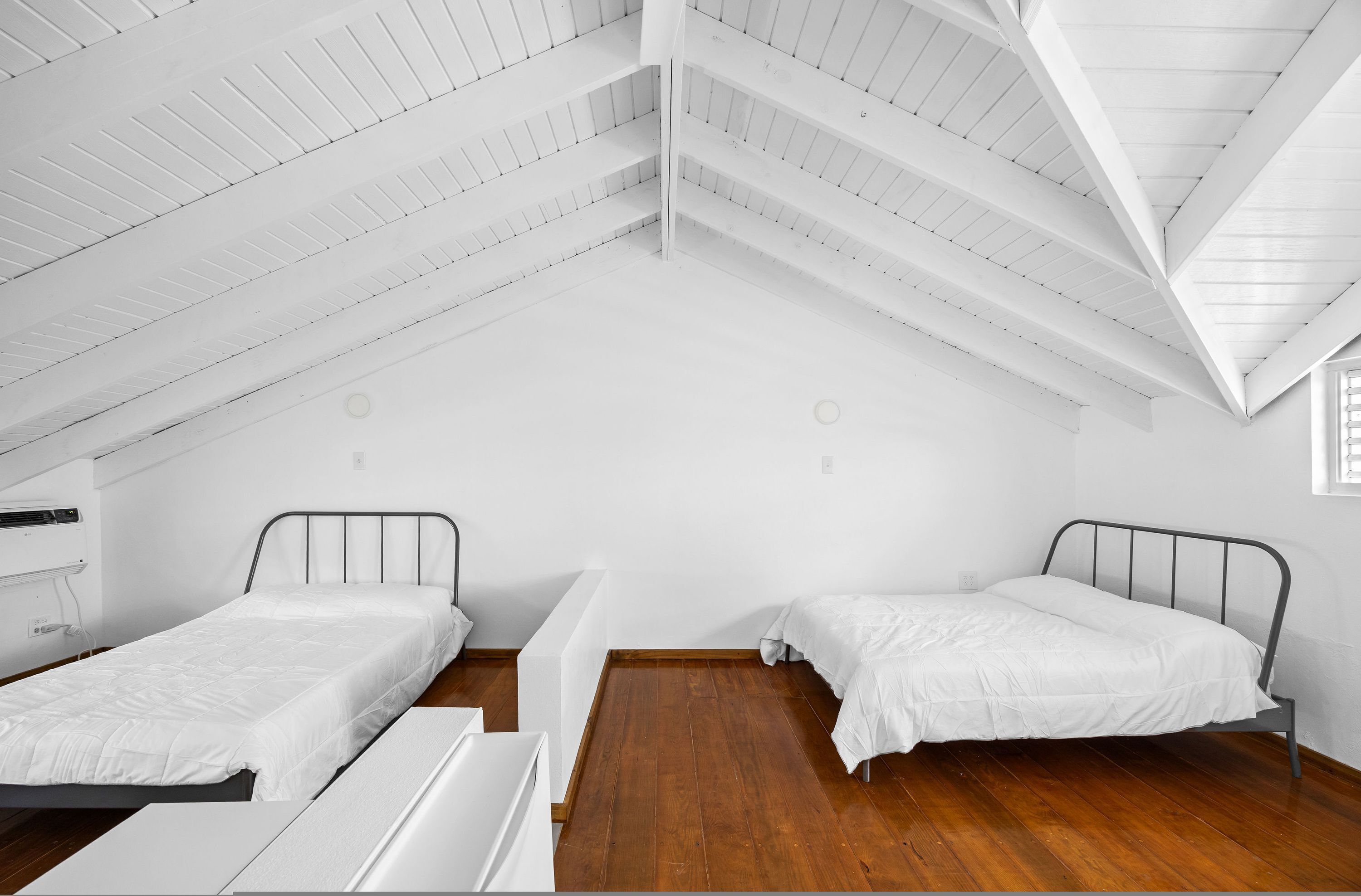 A room with two beds, a wooden floor, white walls, and a sloped ceiling.