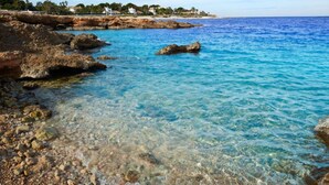 A coastal scene with clear blue waters, rocky shore, and buildings in the background. - Marina A8 With 3 Bedrooms and 2 Bathrooms (Denia)