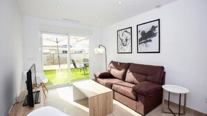 A modern living room with a brown sofa, a wooden coffee table, and a small white side table. There are two black and white framed artworks on the wall. - Marina A2 With 3 Bedrooms and 2 Bathrooms (Denia)