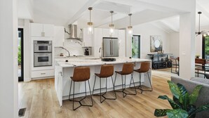A modern kitchen with a central island, bar stools, stainless steel appliances, and pendant lighting. - Sunset Rentals | Planters Wood 48 (Hilton Head Island)