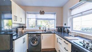 A compact kitchen with a washing machine, a sink, and a window with a view of the outdoors. - Cardiff Gem on Topaz Street - 4 Bedroom House (Cardiff)