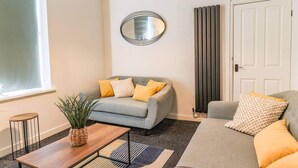 A living room with a grey sofa, a wooden coffee table, and a potted plant. - Cardiff Gem on Topaz Street - 4 Bedroom House (Cardiff)