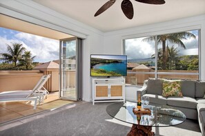Ein modernes Wohnzimmer mit Fernseher, Sofa und Balkon mit Blick auf einen Strand und Palmen.