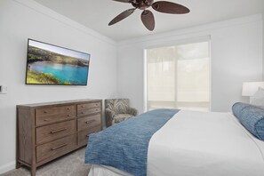 Ein Schlafzimmer mit einem Bett, einem Schminktisch, einem Sessel, einem Deckenventilator und einem großen Fenster.