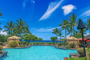 Ein Pool in einer Hotelanlage mit Palmen und Blick auf den Strand.