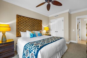Ein Schlafzimmer mit einem großen Bett, einem Deckenventilator, einem hölzernen Kopfteil, zwei Nachttischlampen und einer Tür.