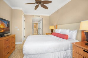 Une chambre d’hôtel équipée d’un lit, d’une télévision, d’un ventilateur de plafond et d’un couloir menant à une salle de bain.