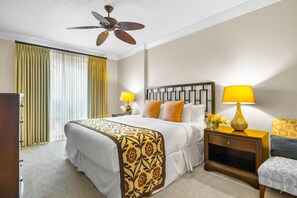 A hotel room with a bed, two bedside tables, a nightstand, a ceiling fan, and a window with curtains.