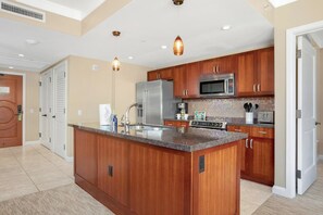 A kitchen with wooden cabinets, stainless steel appliances, a granite countertop, and pendant lighting. - Honua Kai | Ocean View 10 BR, Sleeps 28 | Car Incl. w/ 6+ Nights | HKH ML-1105 by KBM (Lahaina)