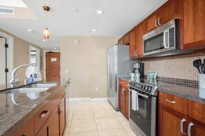 A modern kitchen with wooden cabinets, stainless steel appliances, a granite countertop, and a tiled backsplash.