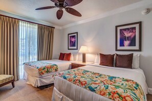A hotel room with two beds, a ceiling fan, a nightstand with a lamp, and two framed pictures on the wall.