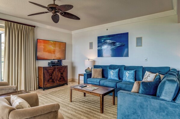 A living room with a blue sofa, a wooden cabinet, a television, and a ceiling fan.