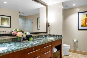 A bathroom with a marble sink, wooden vanity, a large mirror, a toilet, and framed artwork on the wall.