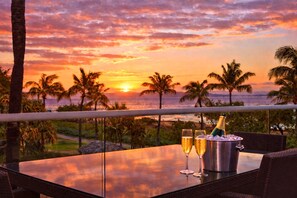 Zonsondergang vanaf een balkon met een tafel, twee champagneglazen en een champagnefles.